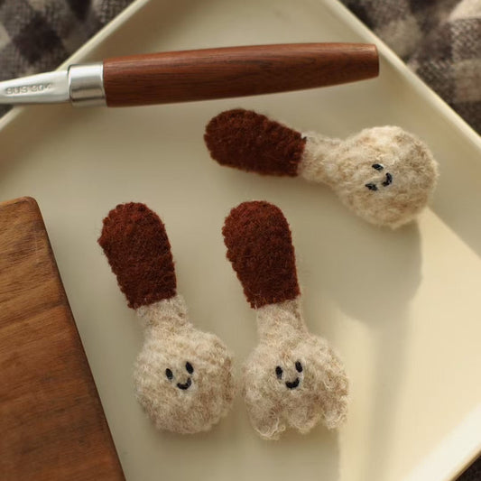Two small crocheted matchstick characters on a white plate with a wooden-handled tool.