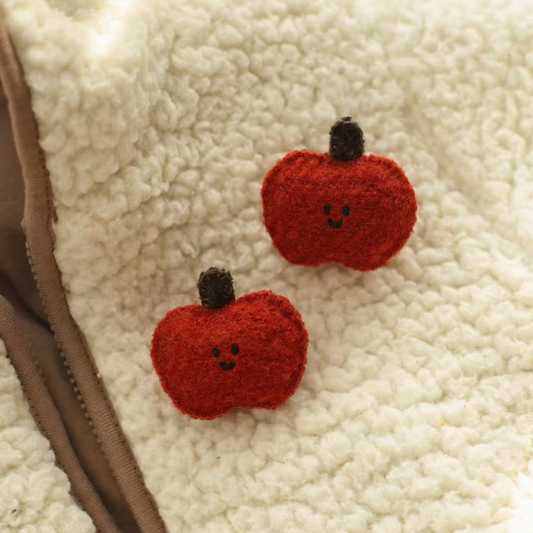 Two red red-shaped earrings on a textured beige surface