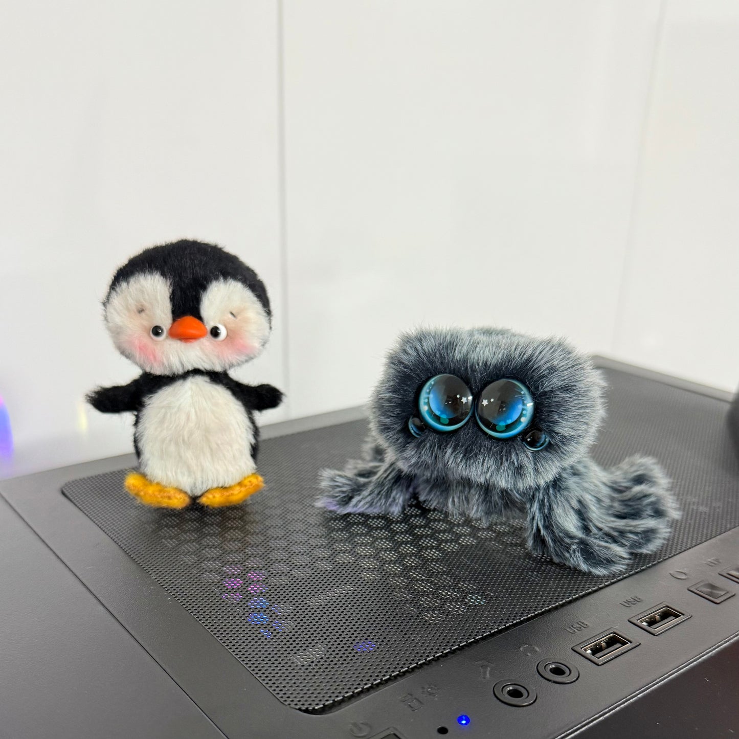 Two plush toys, a penguin and a gray creature with large eyes, on a computer desk.