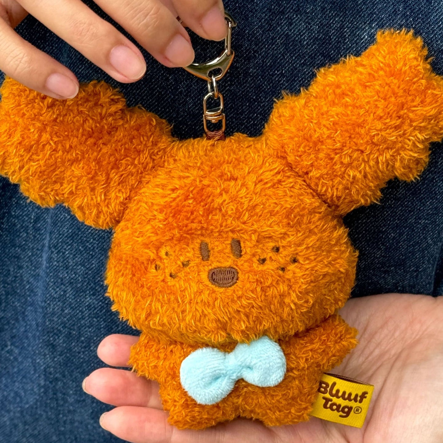 Orange plush keychain with a blue bow tie held by a person against a denim background
