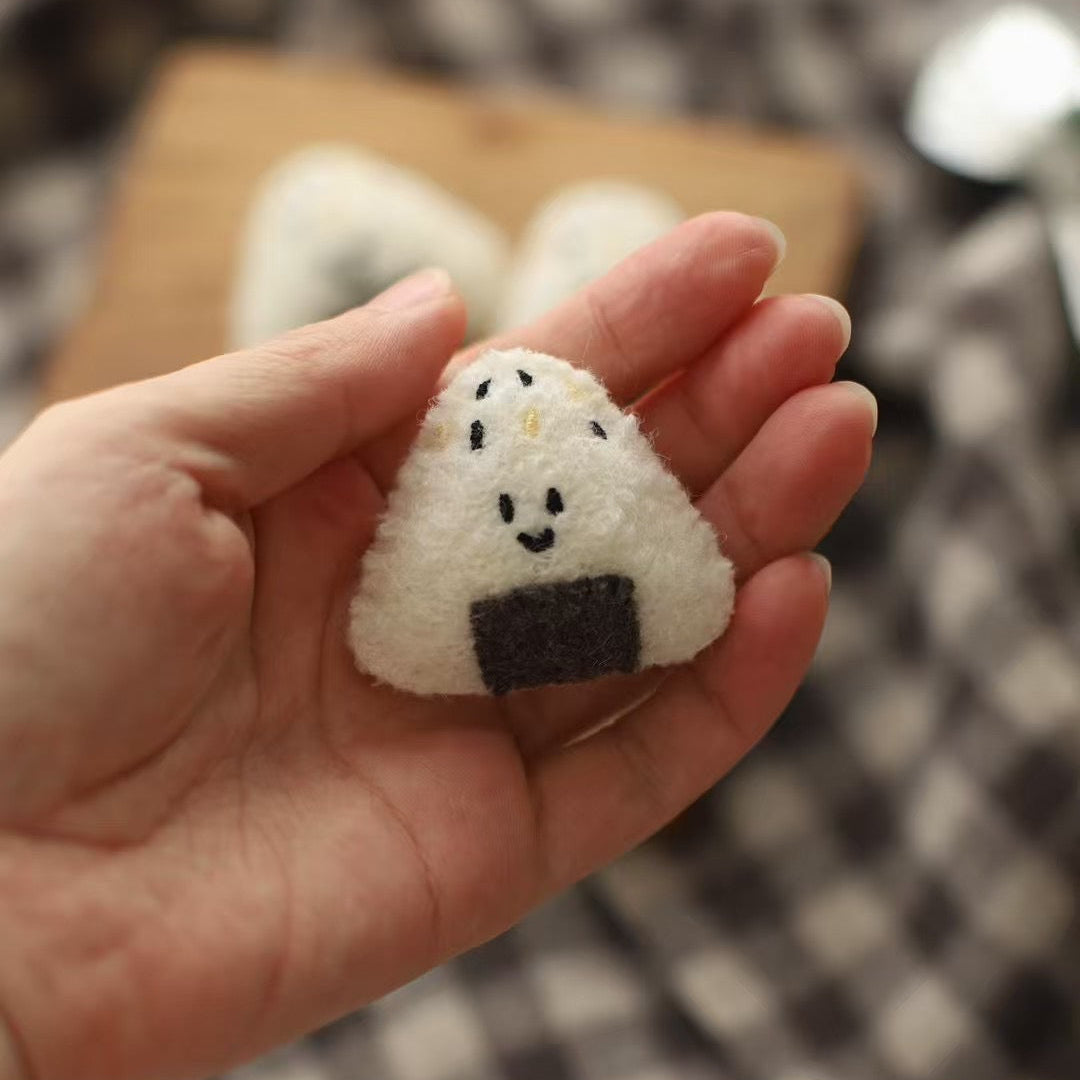 Hand holding a small rice ball-shaped plush toy on a checkered background