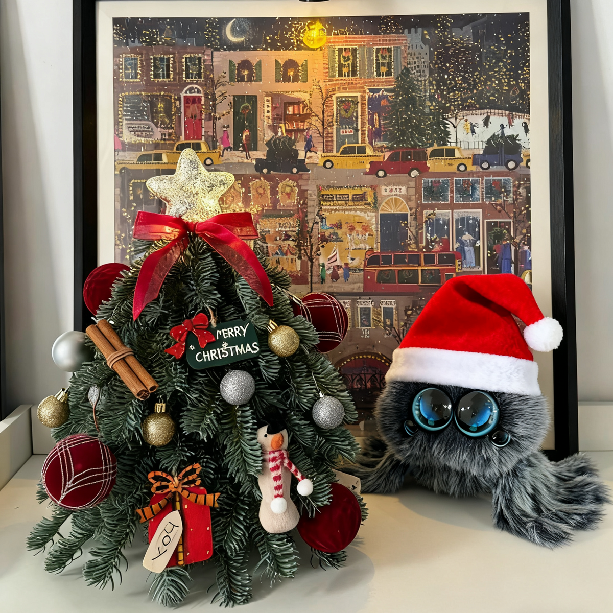 Decorative Christmas tree with ornaments and a Santa hat on a table in front of a framed artwork.