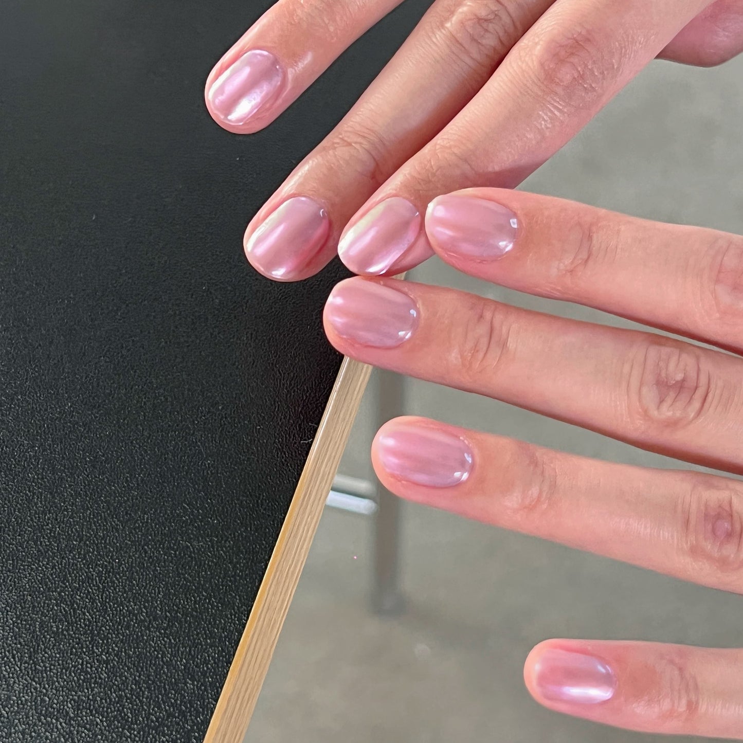 Close-up of a hand with pink nail polish on a black surface