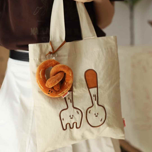 Tote bag with cartoon designs of a pretzel and a soft toy hanging from it.