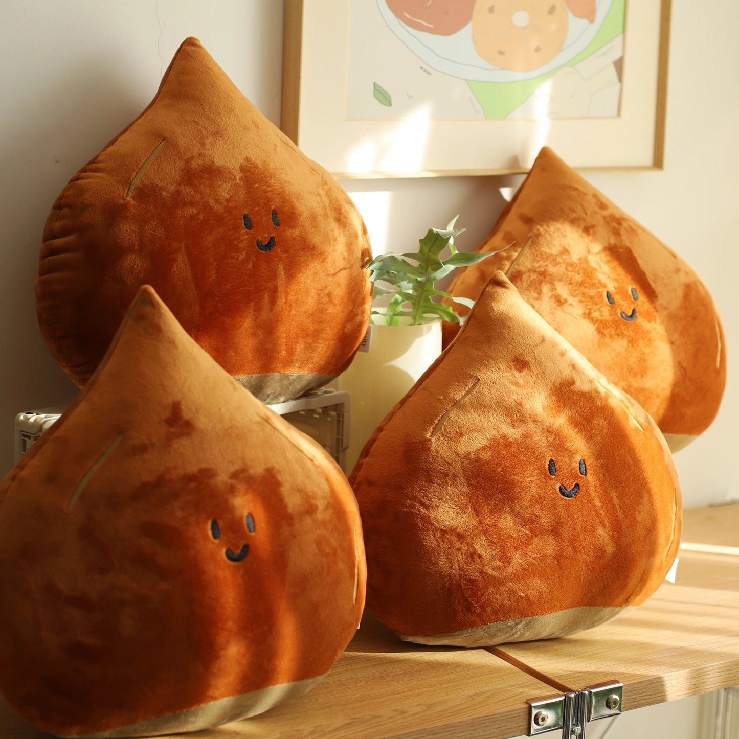 Three brown plush pillows with smiling faces on a wooden surface, with a framed picture in the background.
