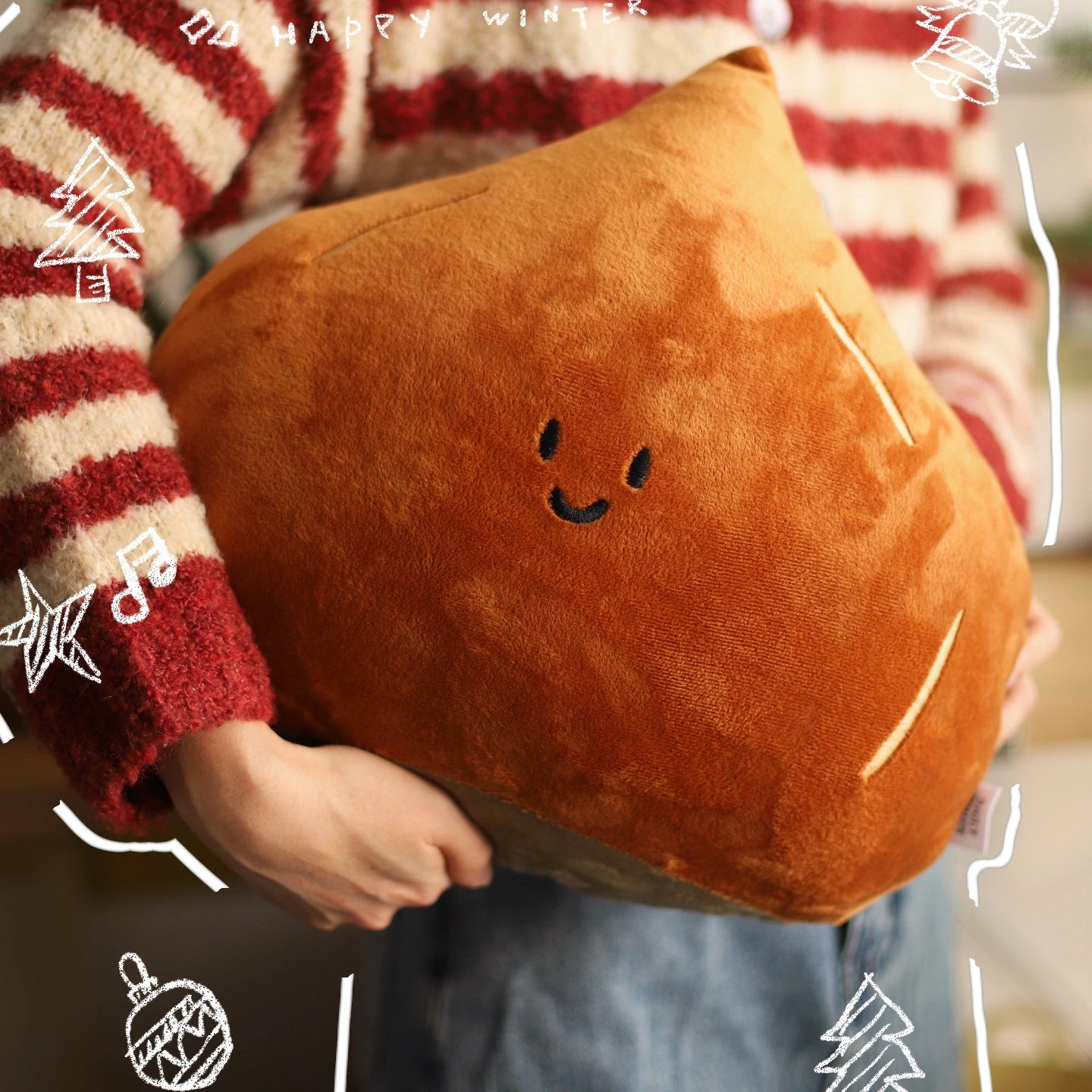Person holding a brown cushion with a smiley face design, wearing a red and white striped sweater.