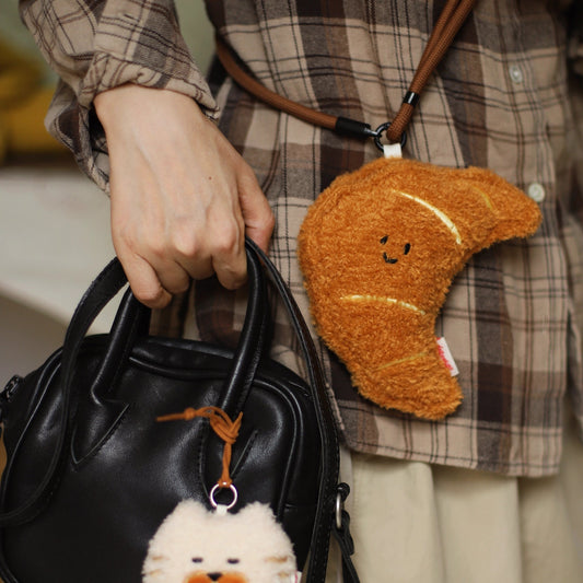 Person holding a black handbag with a cute plush keychain, wearing a plaid shirt and beige pants.