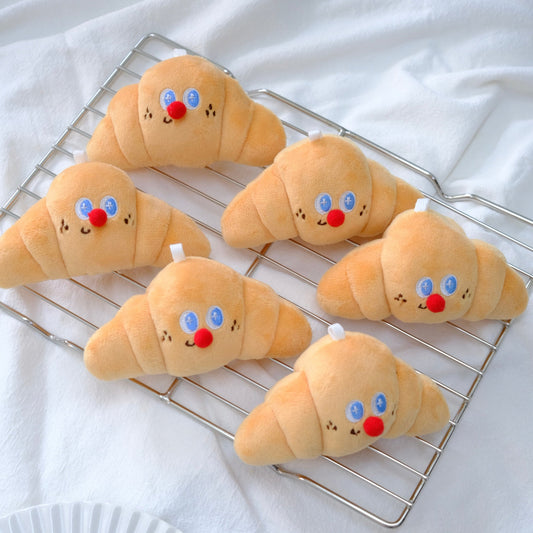 Plush croissants with facial expressions on a cooling rack