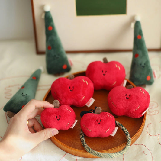 Red plush apples with smiling faces on a wooden plate, surrounded by green trees with red dots.