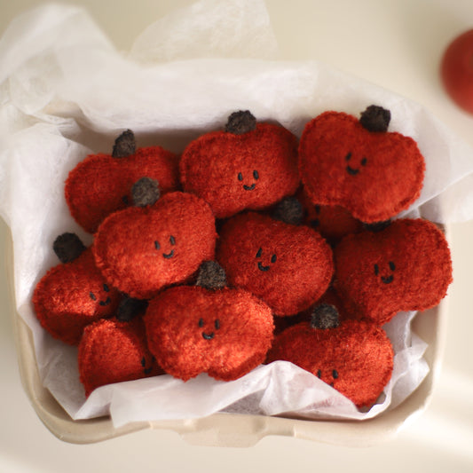 Red felt pumpkins with smiling faces on a white surface