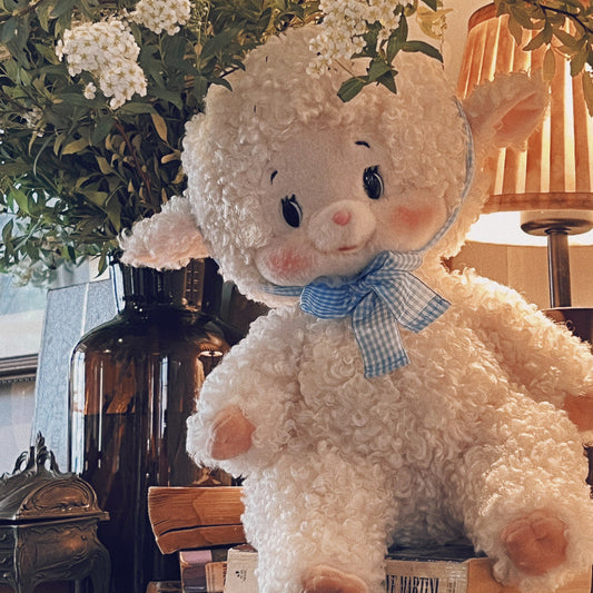 Plush lamb toy with a bow tie on a table with decorative items and plants.