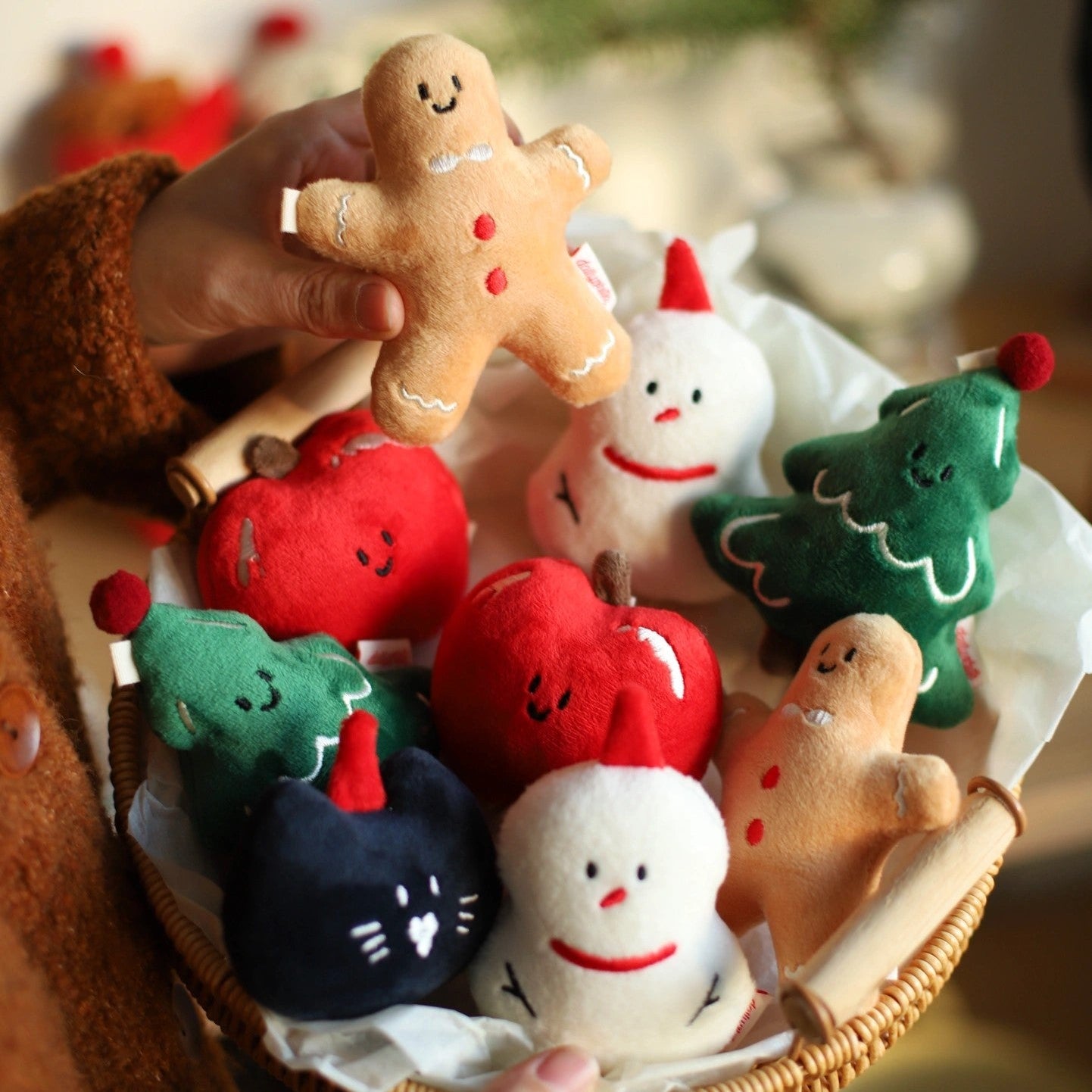 Hand holding a plush gingerbread man toy with other Christmas-themed plush toys in a basket.