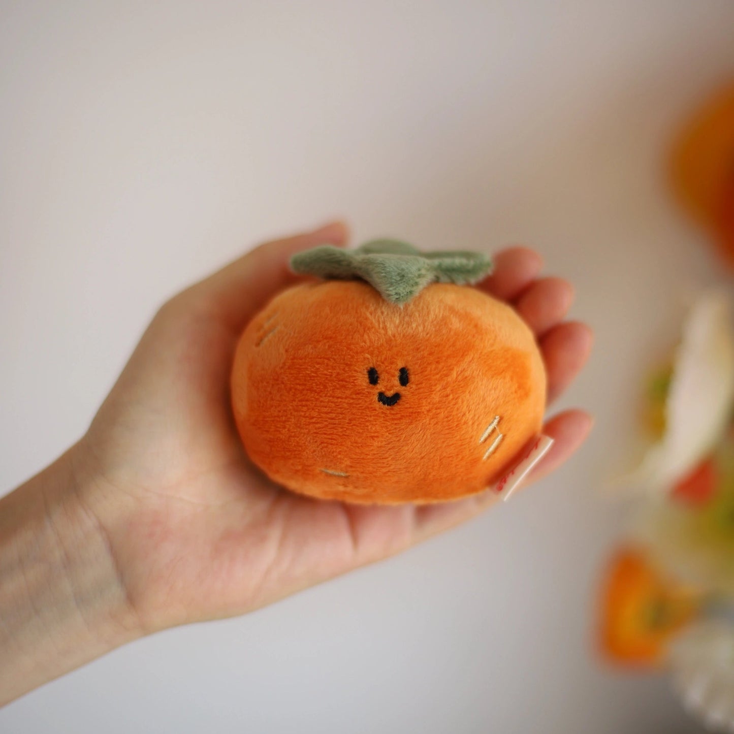 Hand holding a small plush pumpkin with a smiley face against a plain background