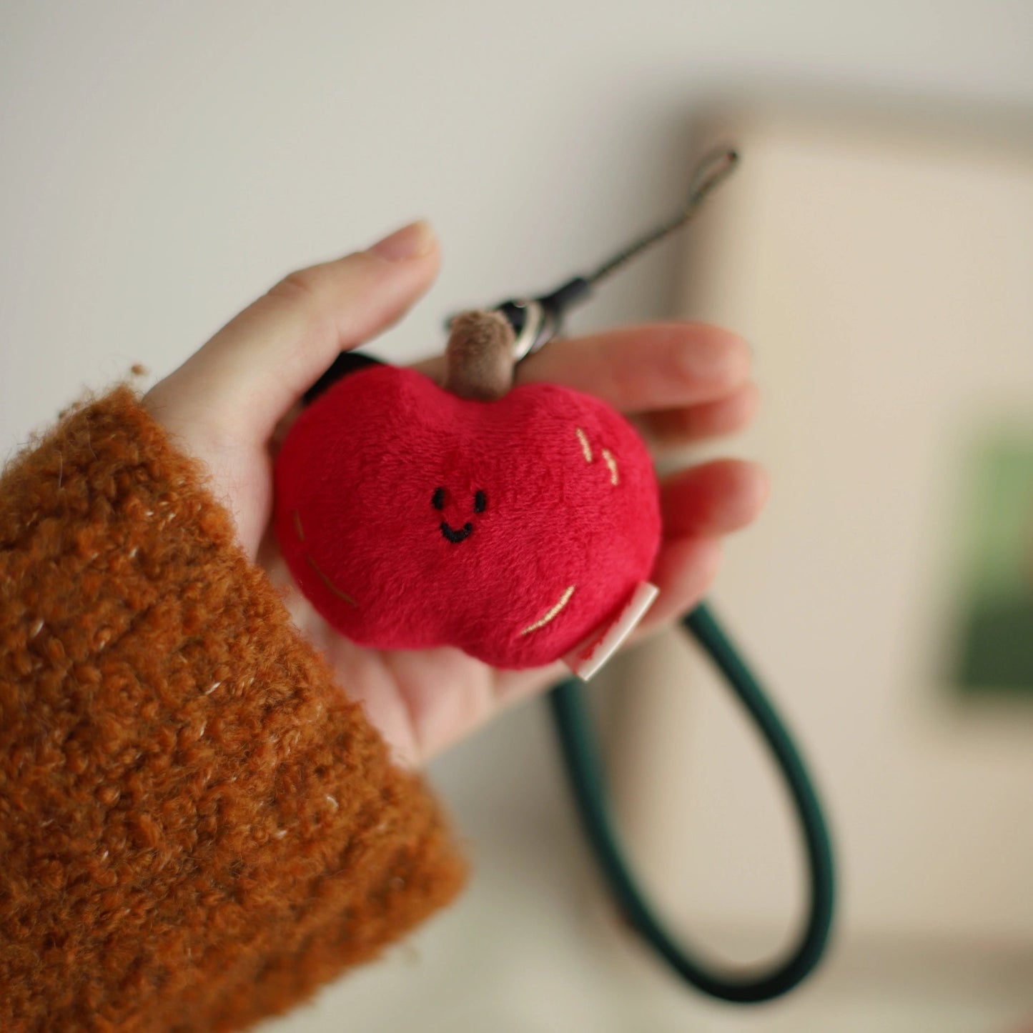Hand holding a red plush apple with a smiling face against a blurred background