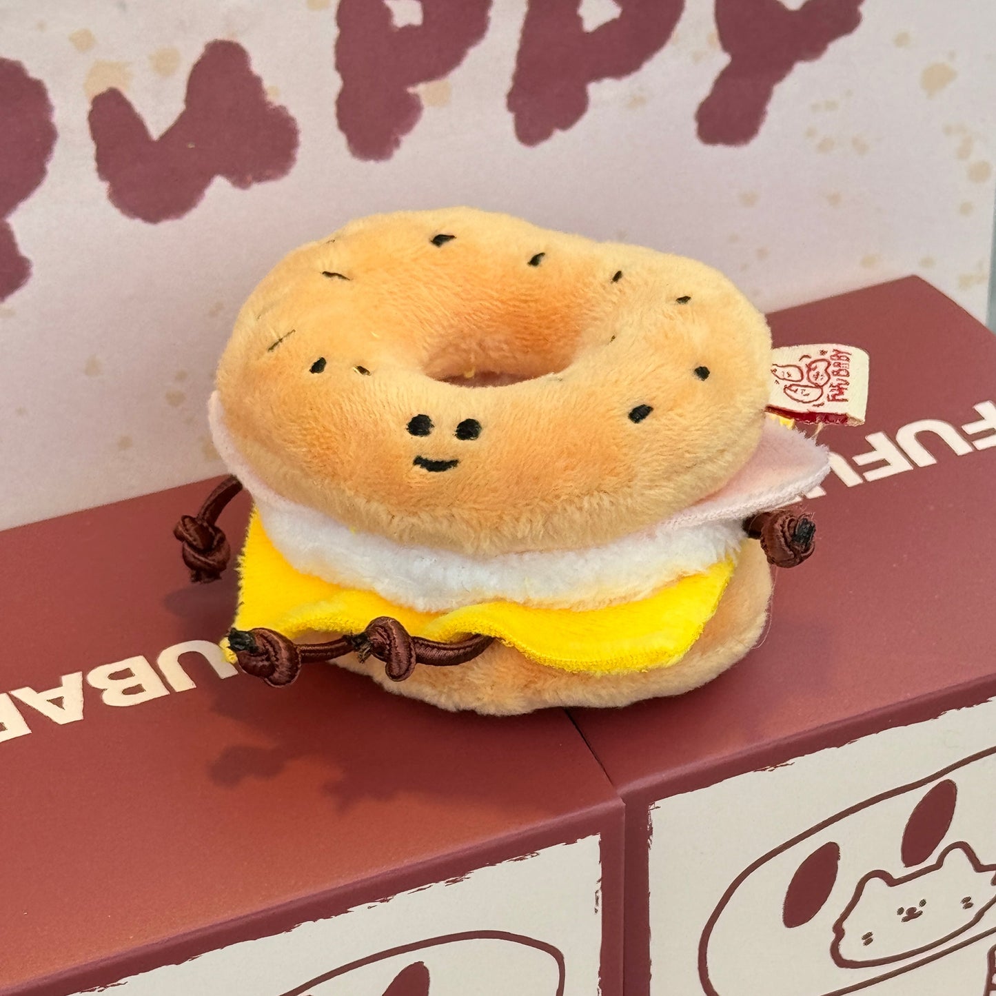 Plush toy resembling a bagel with cream cheese and jelly on a branded box.