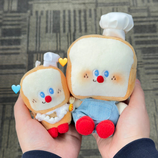 Two plush toys shaped like slices of bread with cartoon faces held in a hand against a textured gray background.