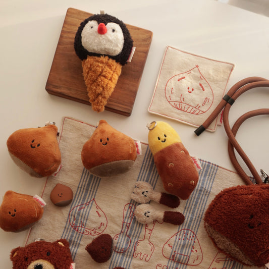Collection of plush toys shaped like buns and penguins on a white surface with a wooden board.