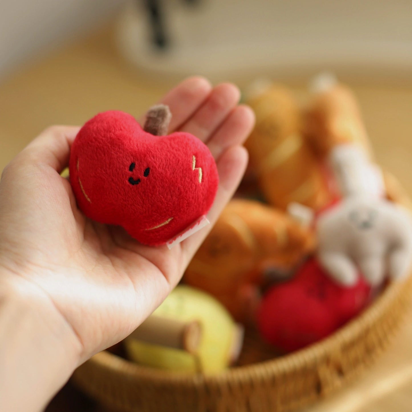 Red plush apple held in a hand with a blurred basket of toys in the background