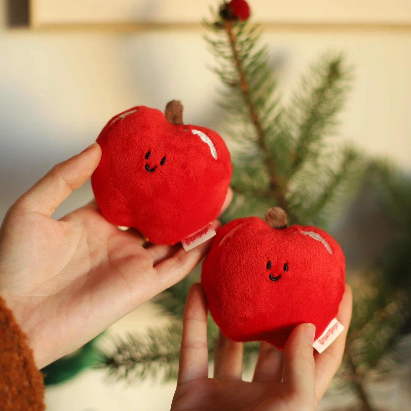 Red plush apples with smiling faces held by a person against a blurred green background
