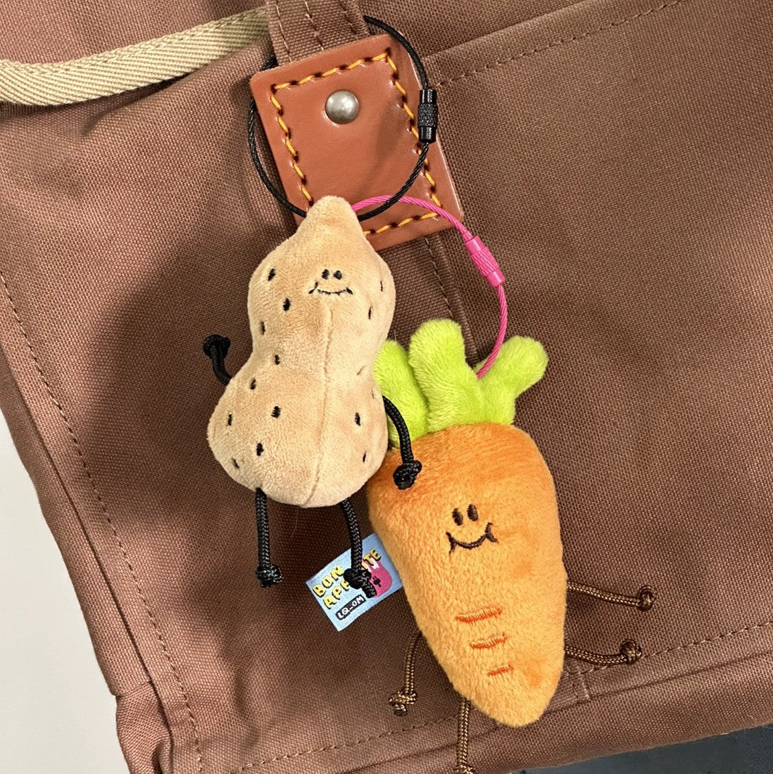 Plush keychain shaped like a carrot and a peanut attached to a brown bag.