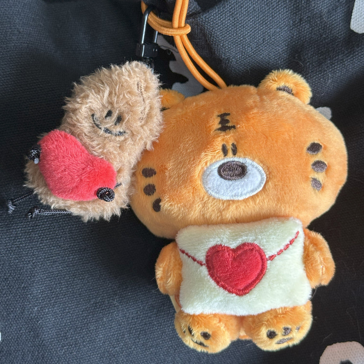 Two plush toys, a peanut and a tiger, with heart designs on a dark surface.