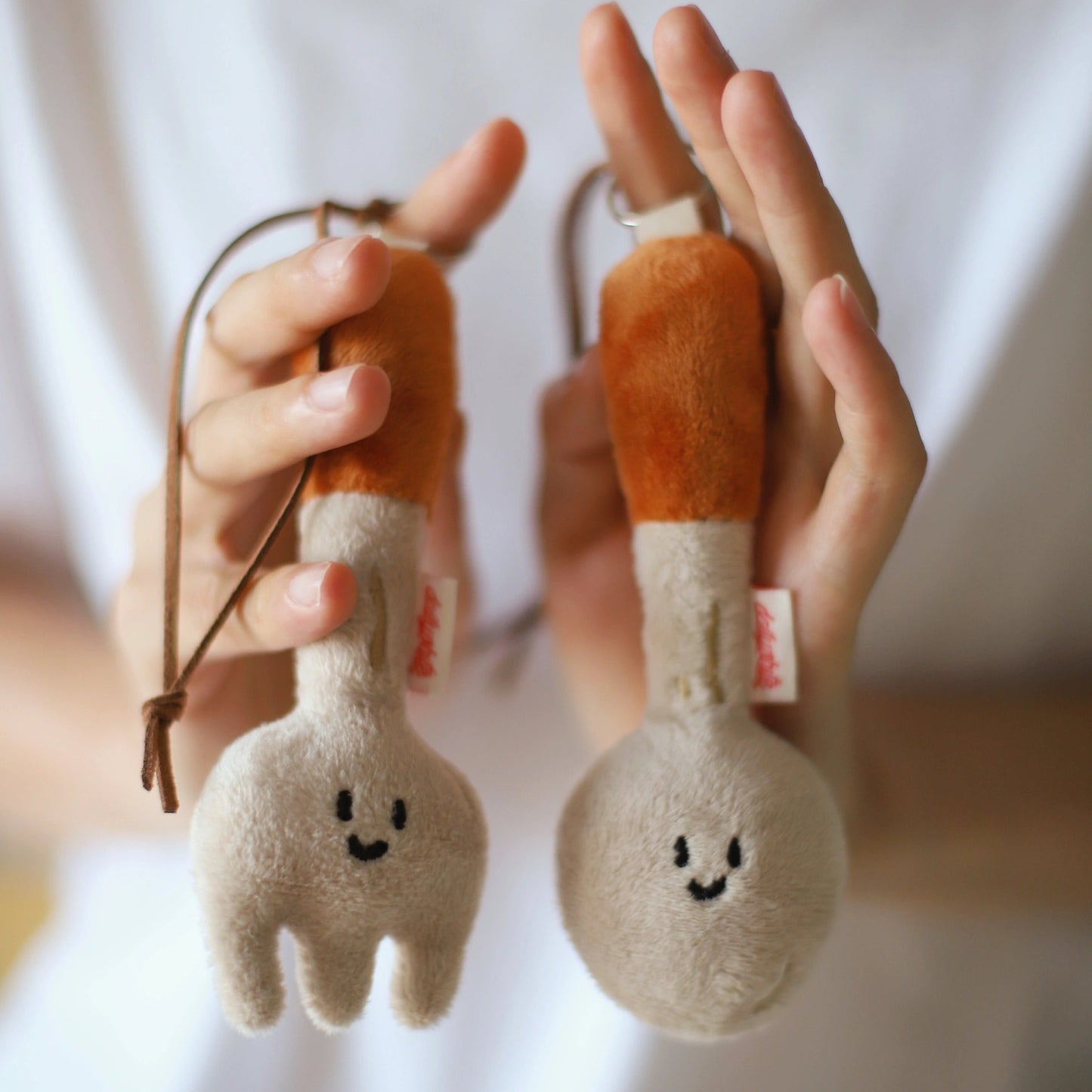 Two plush keychains shaped like a spoon and a fork held in hands against a white background.