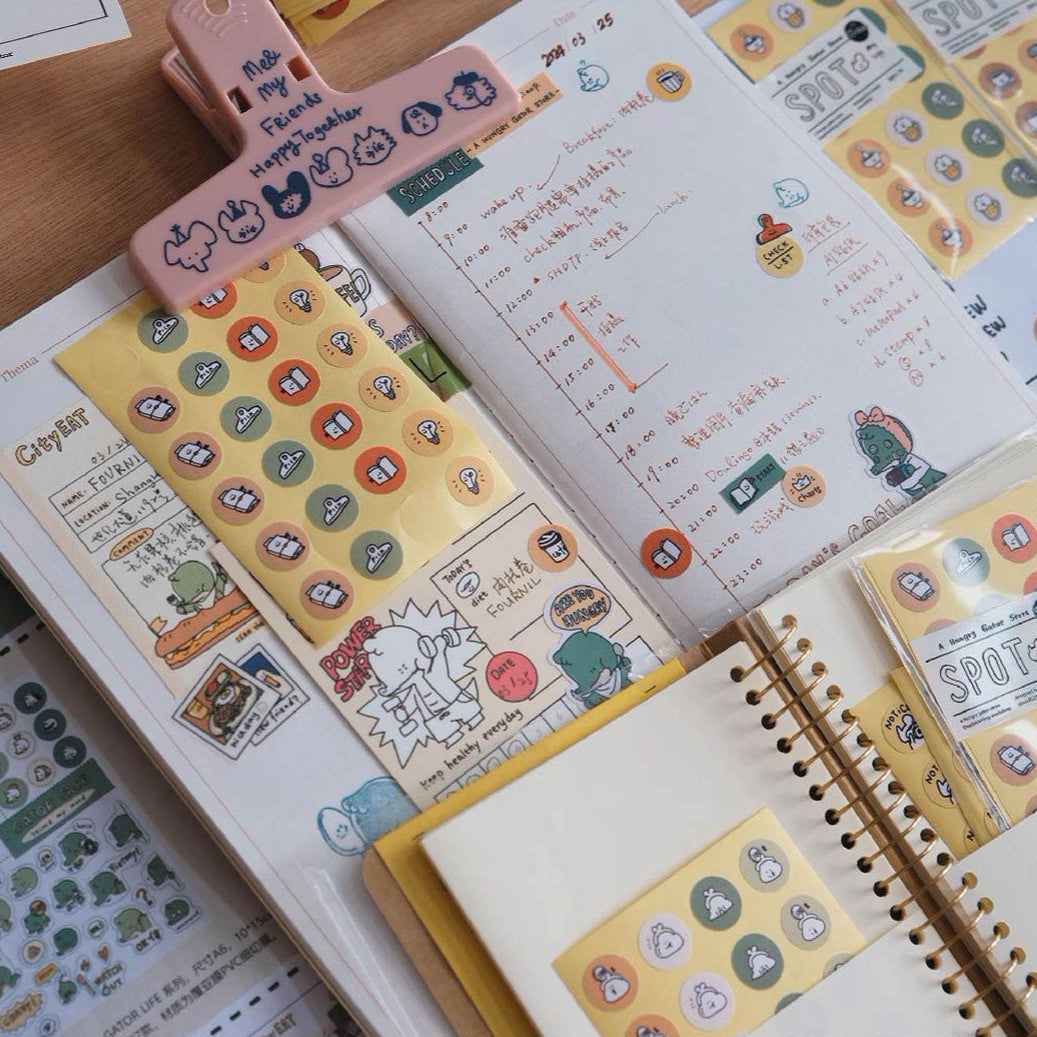Open notebook with stickers and a pink clip on a wooden surface