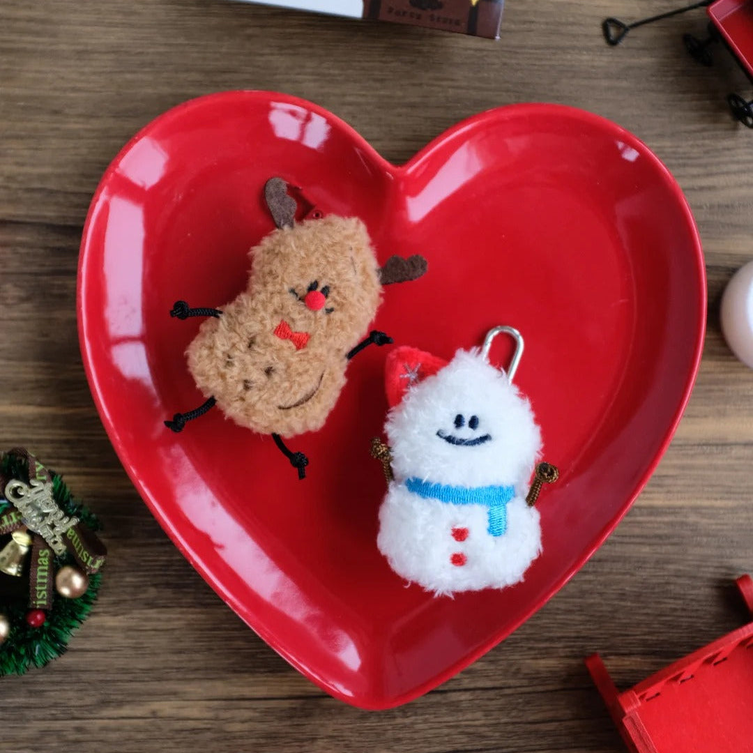 Heart-shaped red dish with Christmas-themed plush toys on a wooden surface.