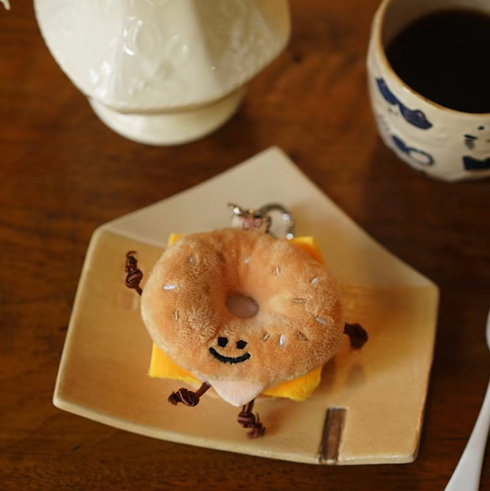 Bagel with cartoon face on a plate with a cup of coffee and vase in the background.