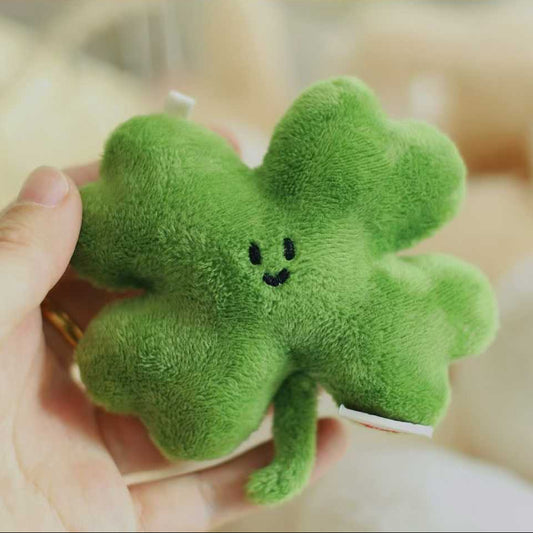 Green plush four-leaf clover held by a hand against a blurred background