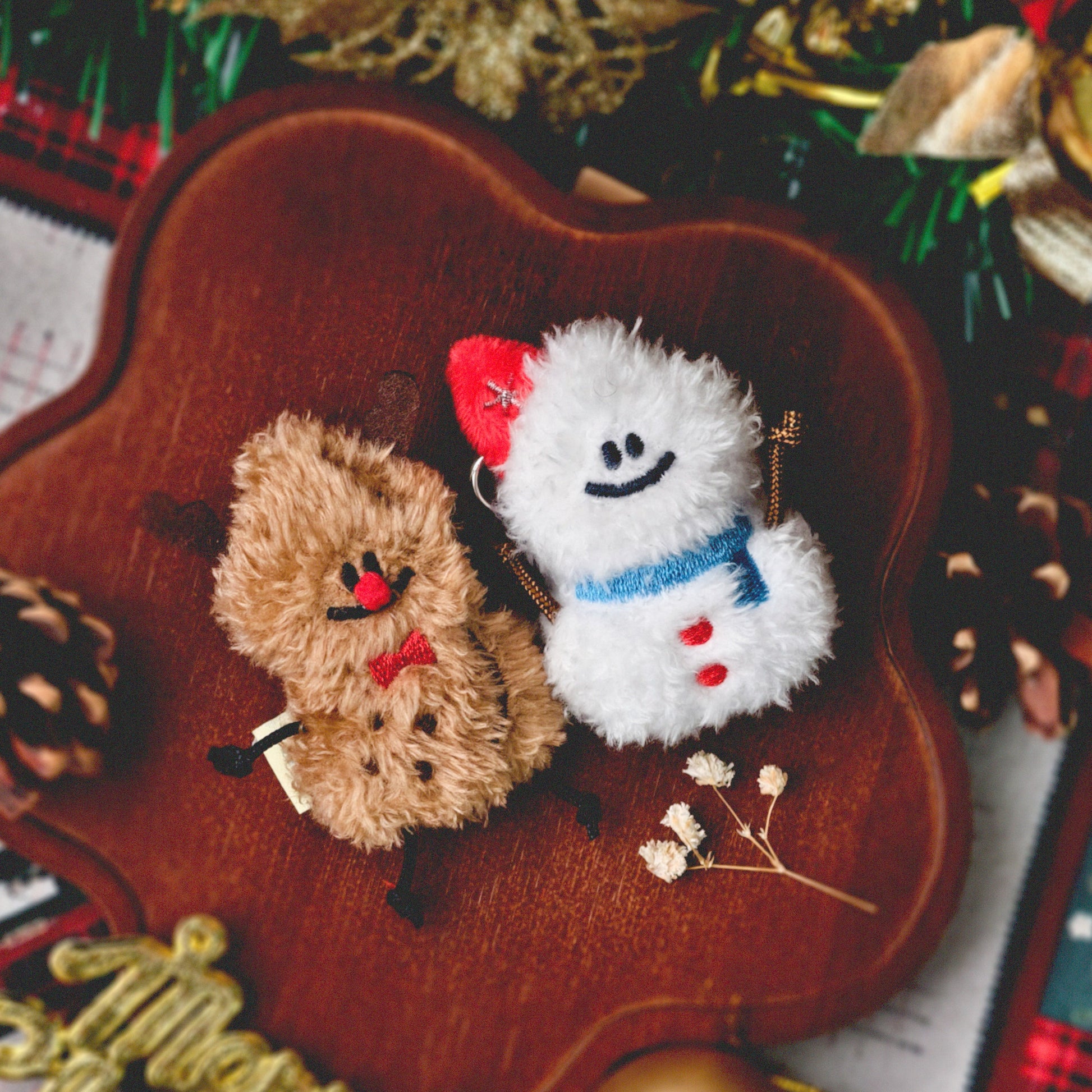 Two small plush toys, one brown and one white with a red hat, on a wooden surface with Christmas decorations.
