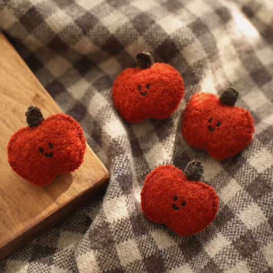 Three red apple-shaped brooches on a checkered fabric background