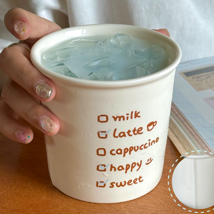 White mug with text holding a drink, on a wooden surface with a blurred background