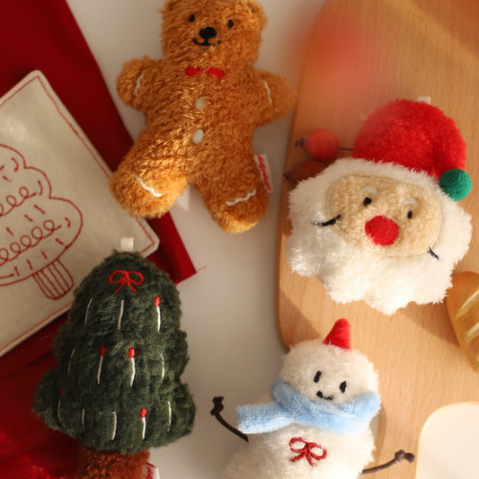 Set of Christmas-themed plush toys including a bear, gingerbread man, tree, and snowman on a wooden surface.