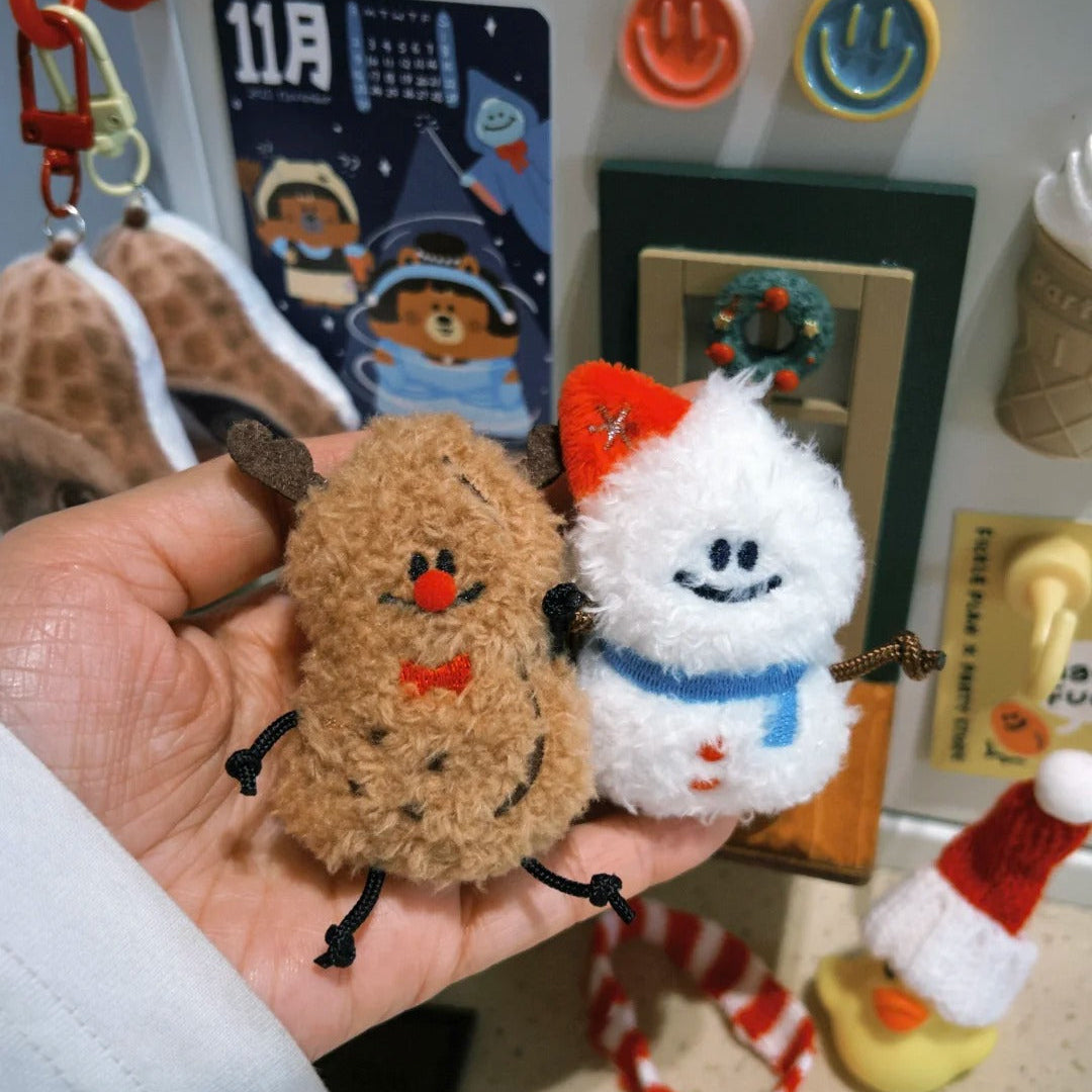 Hand holding two small plush toys, one brown and one white with red accents, in front of a wall with various decorations.
