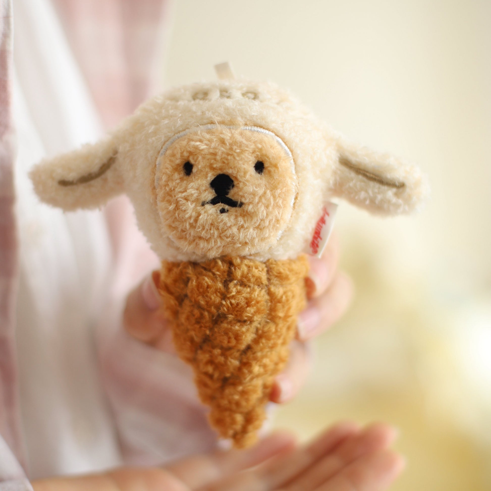 Small plush toy shaped like a sheep ice cream cone held in hands against a blurred background