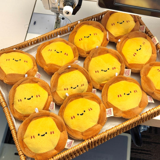 Plush toys resembling eggs with smiley faces on a sewing machine.