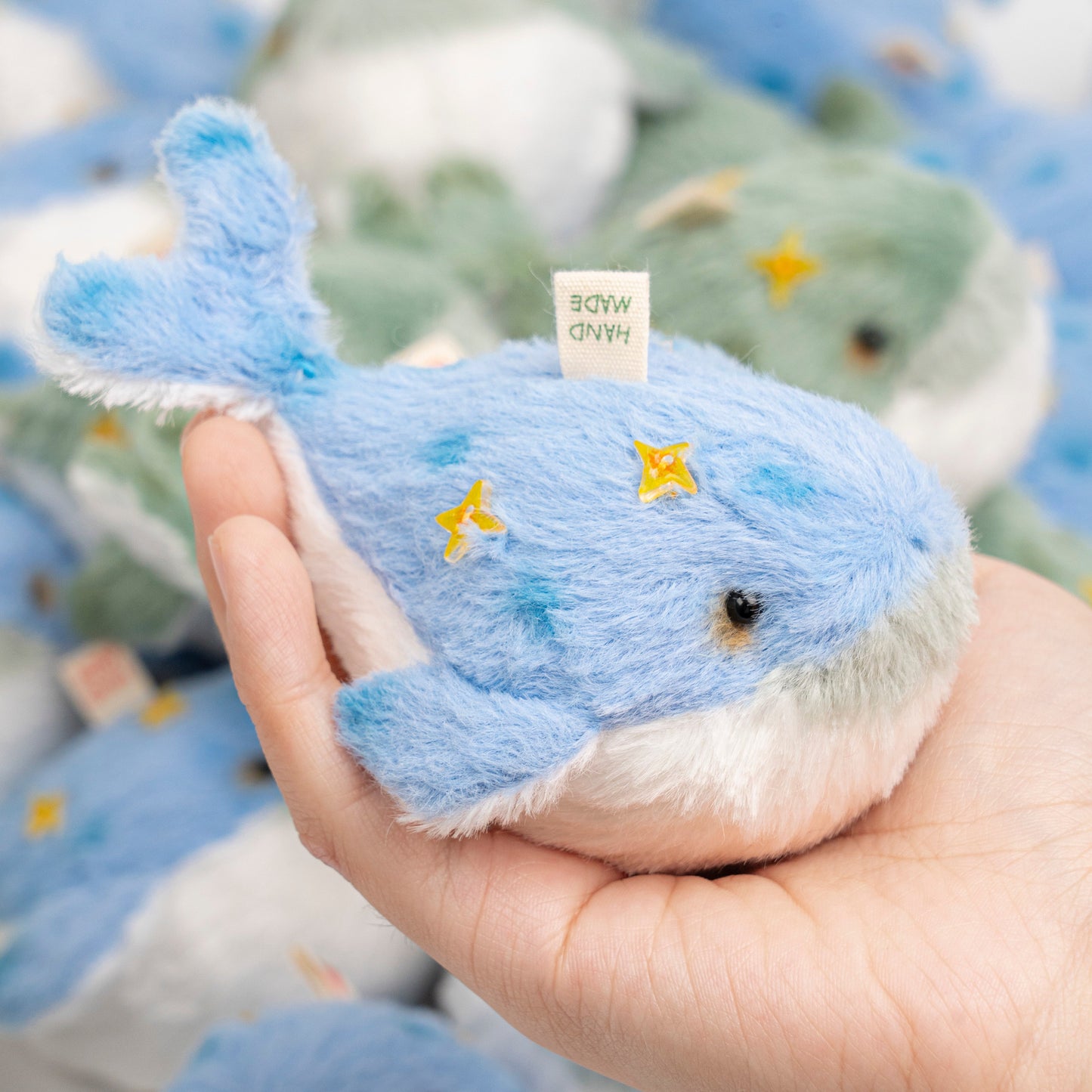 Hand holding a blue plush whale toy with a blurred background of similar toys.