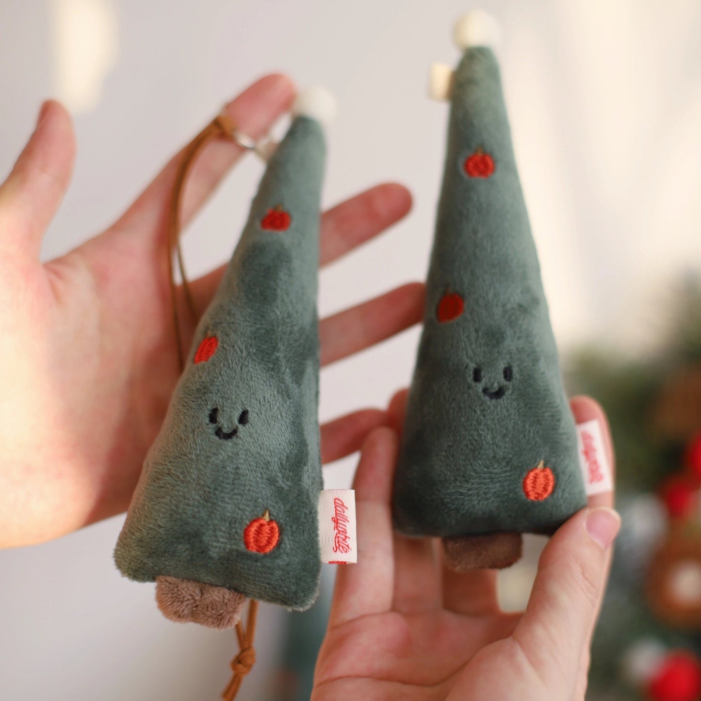 Two small green felt Christmas trees with red dots held by a hand against a blurred background.