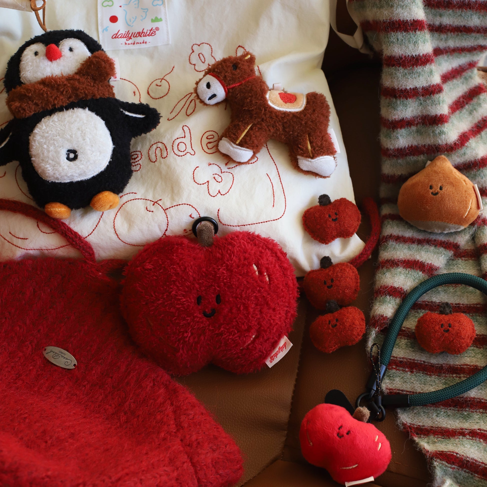 Collection of plush toys including a penguin, bear, and heart-shaped items on a striped fabric background.
