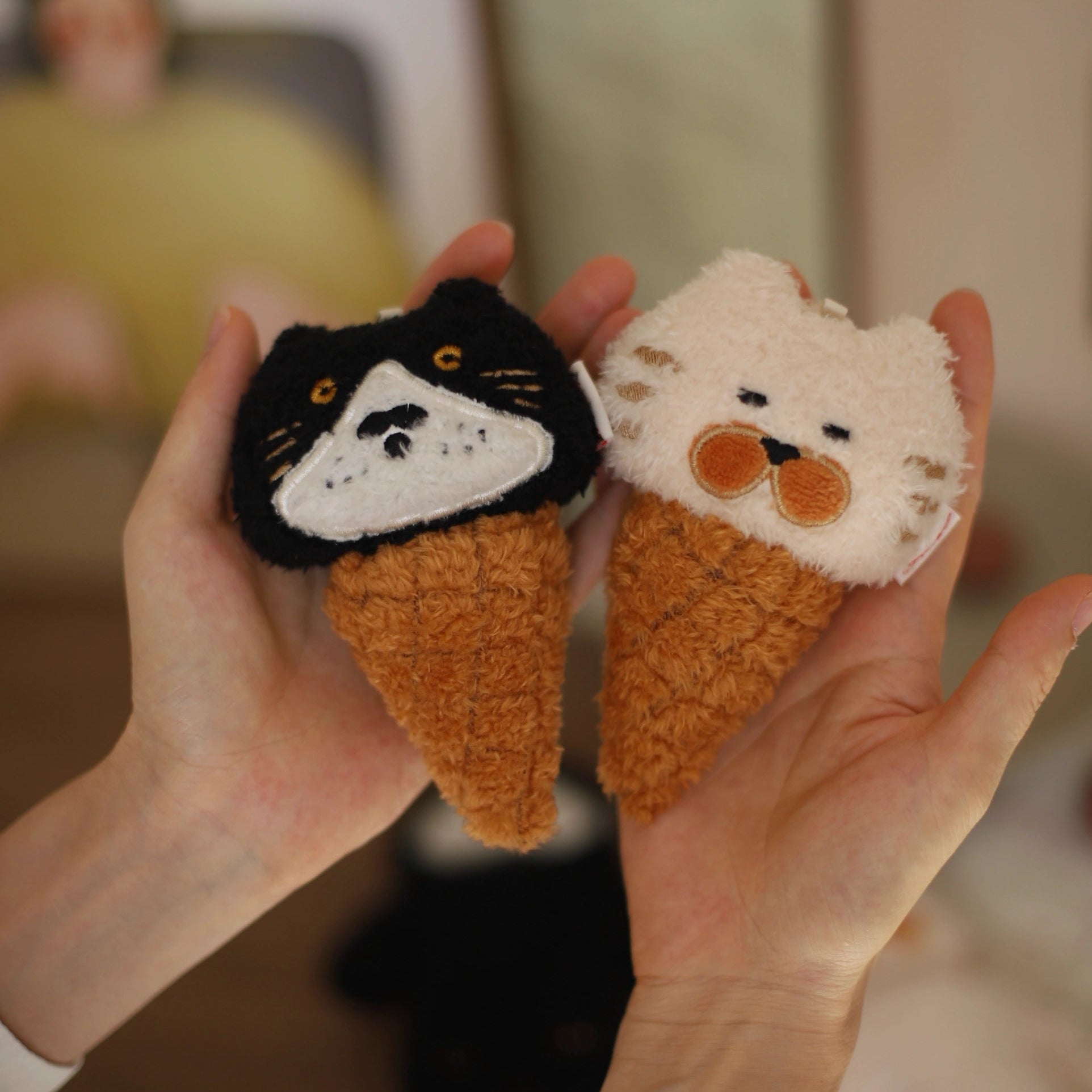 Two plush toys shaped like cats held in hands with a blurred background
