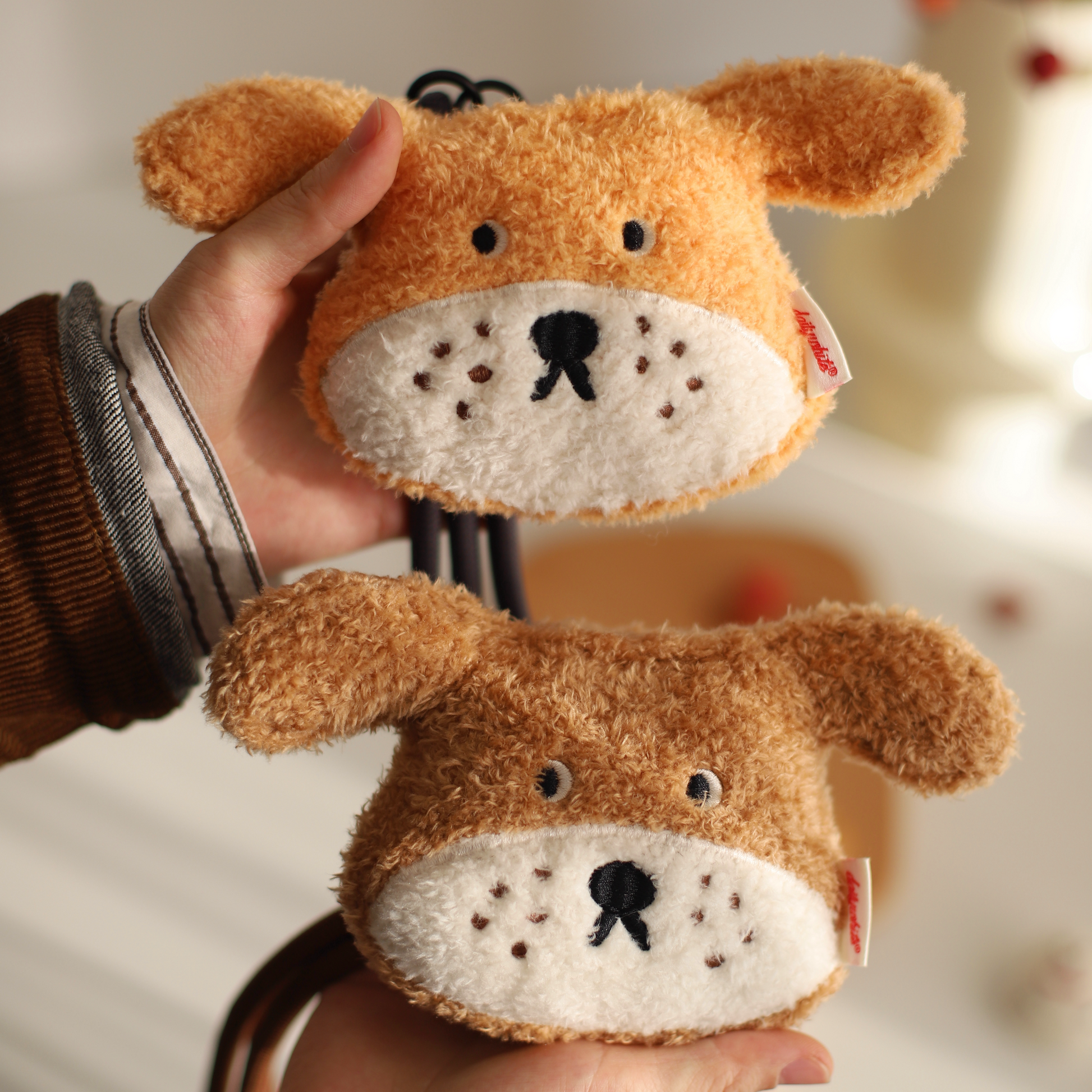 Two plush dog toys held in hands with a blurred background