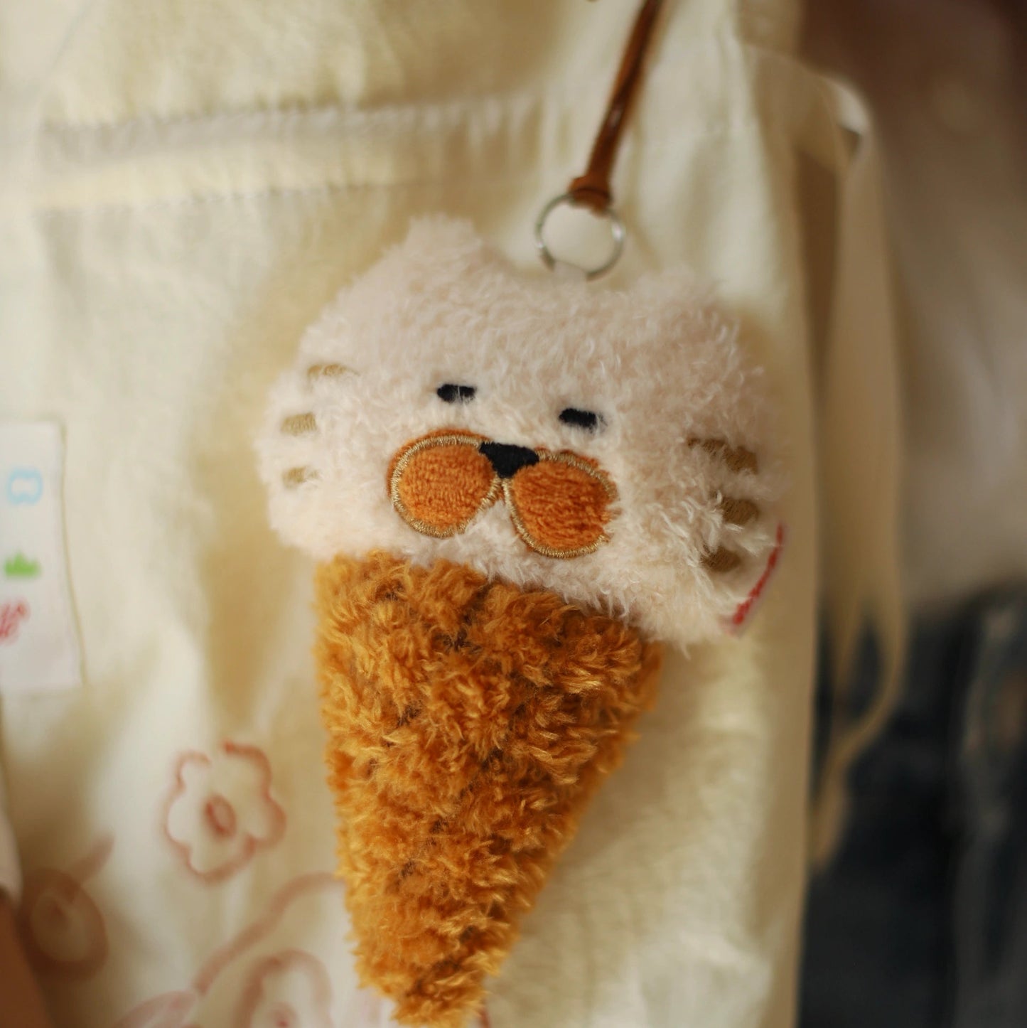 Fuzzy ice cream cone keychain with a face on a light-colored fabric background