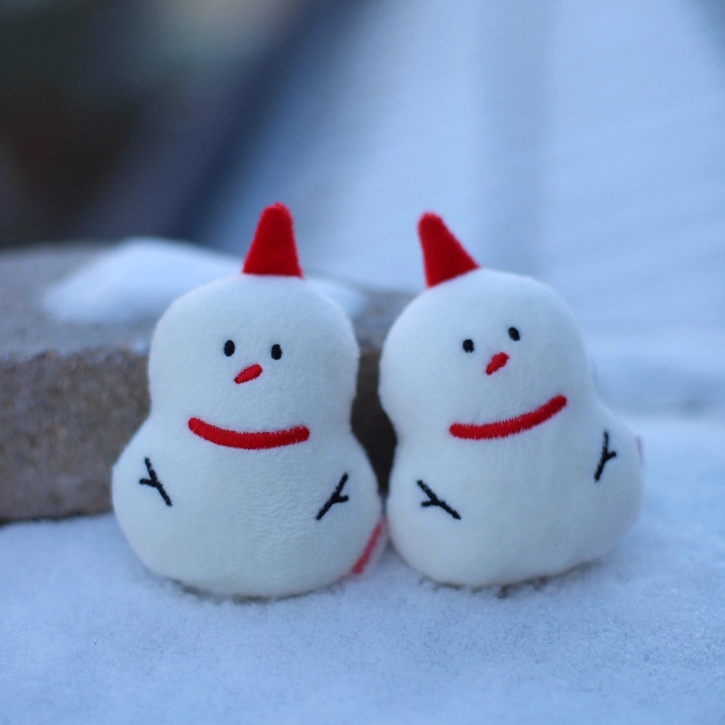 Two small snowmen with red hats and carrot noses on a snowy surface.