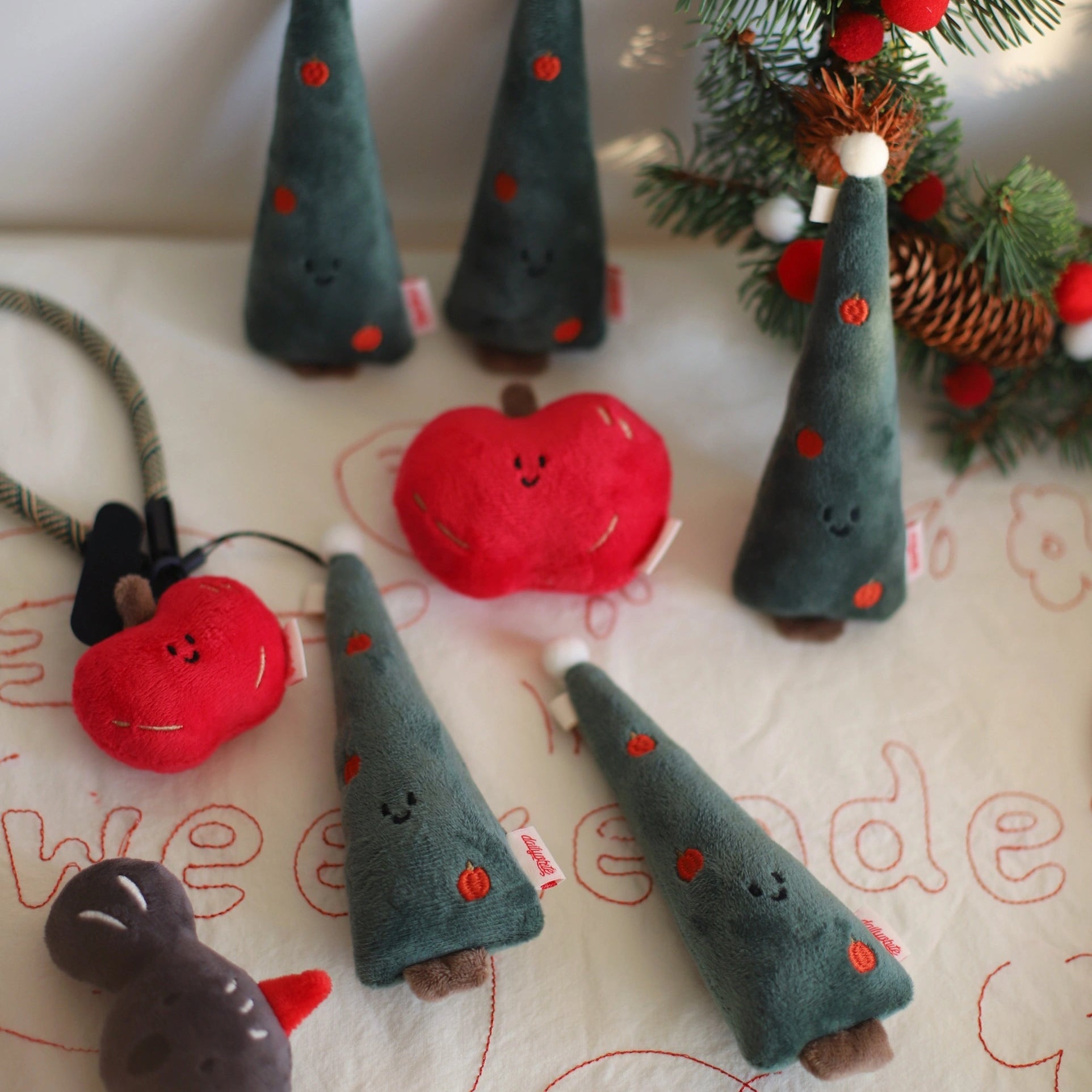 Felt Christmas tree ornaments and a red apple with a face on a decorative surface.