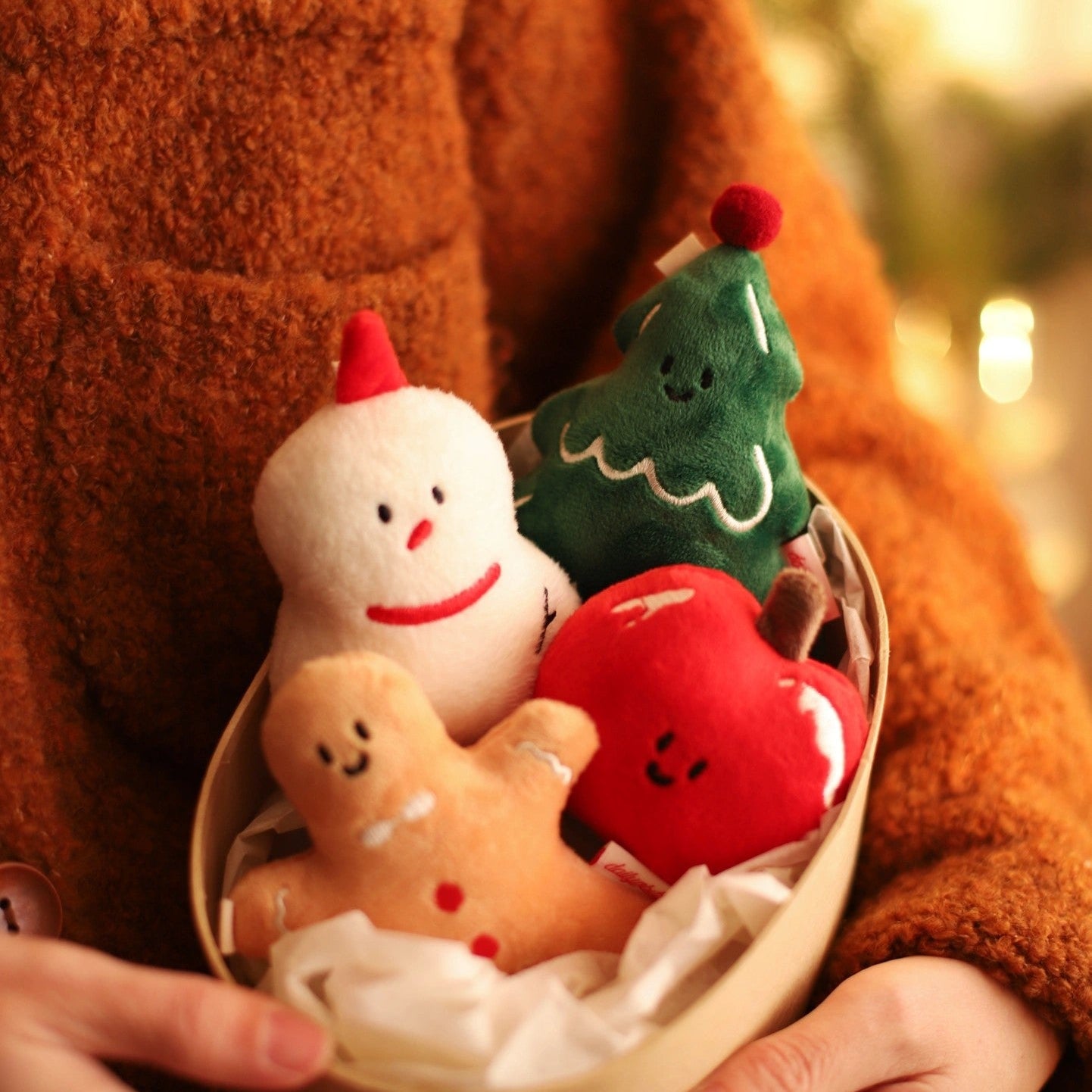 Person holding a small bowl with Christmas-themed plush toys against a blurred background.