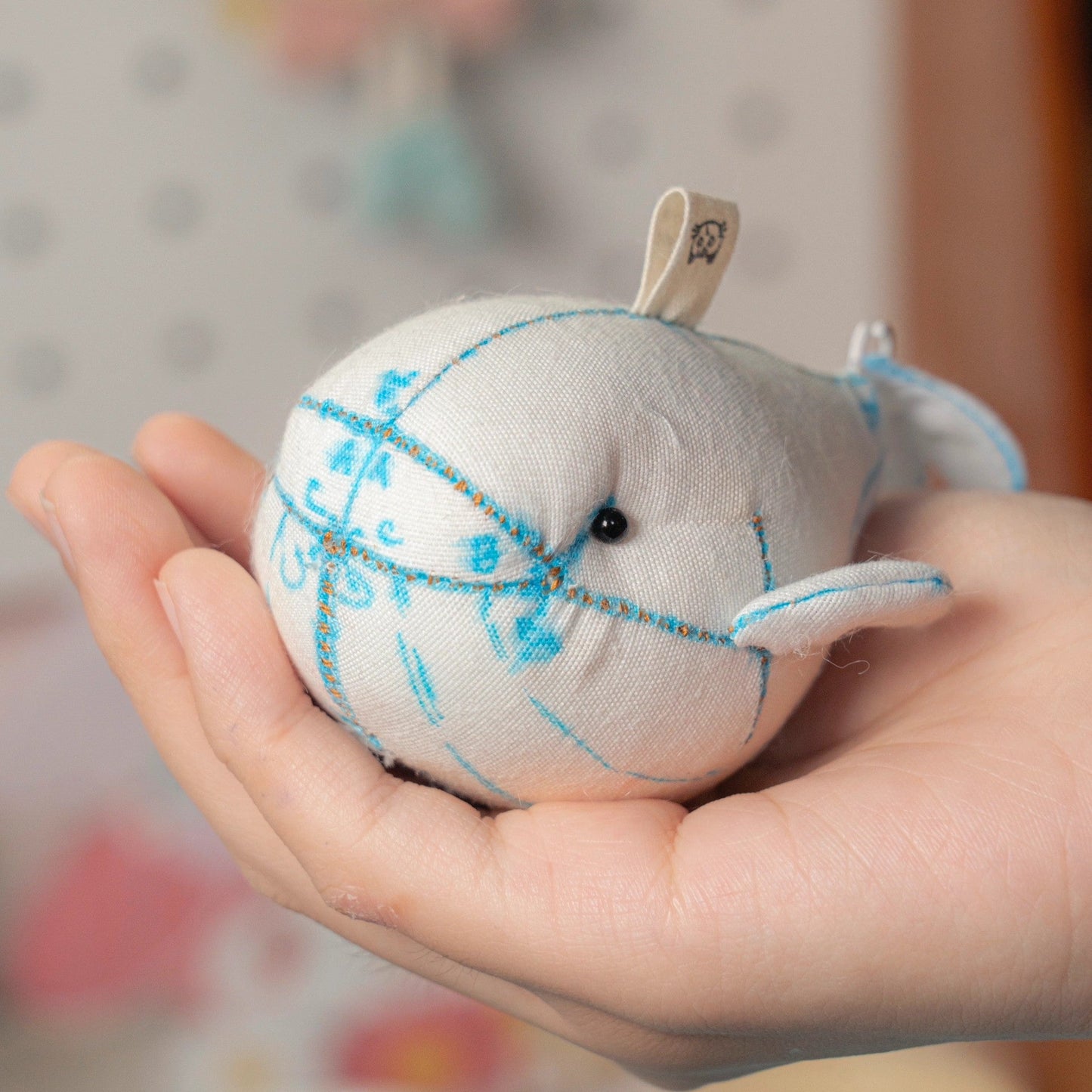 Hand holding a small plush whale toy with blue stitching against a blurred background