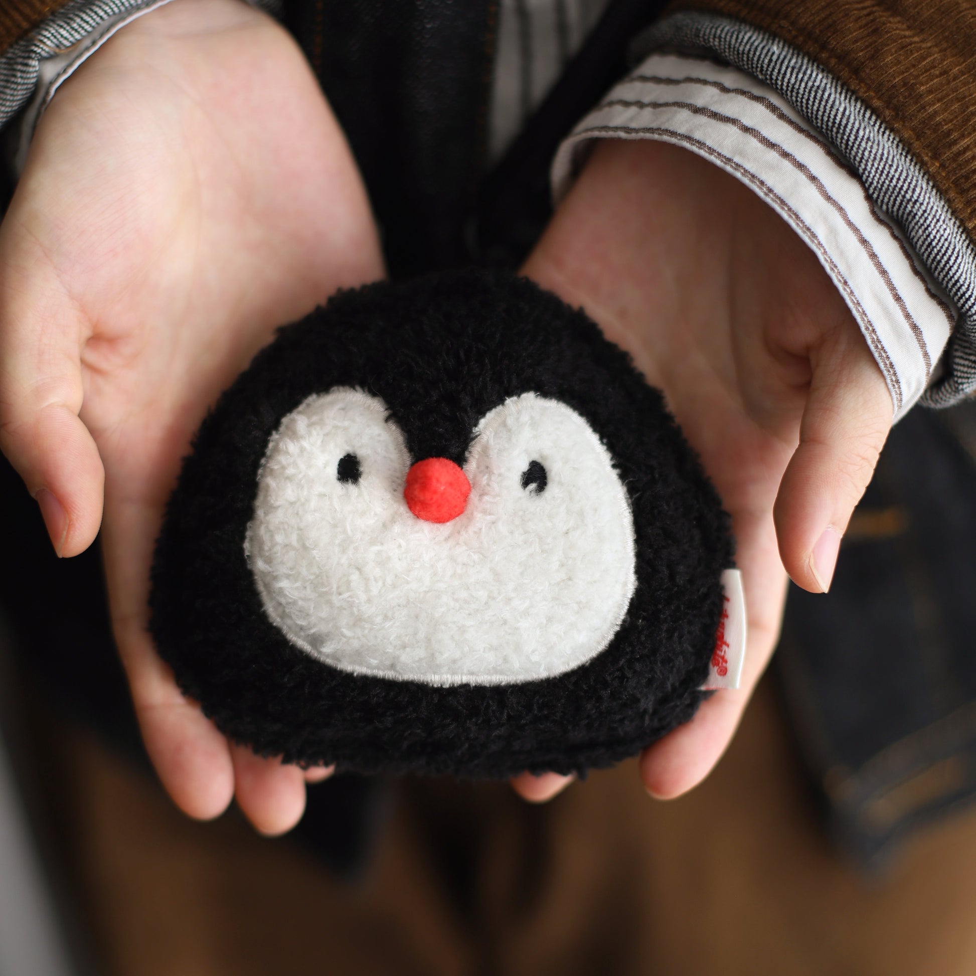 Person holding a black plush toy with a penguin face
