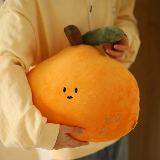 Person holding a plush orange pillow with a face design.
