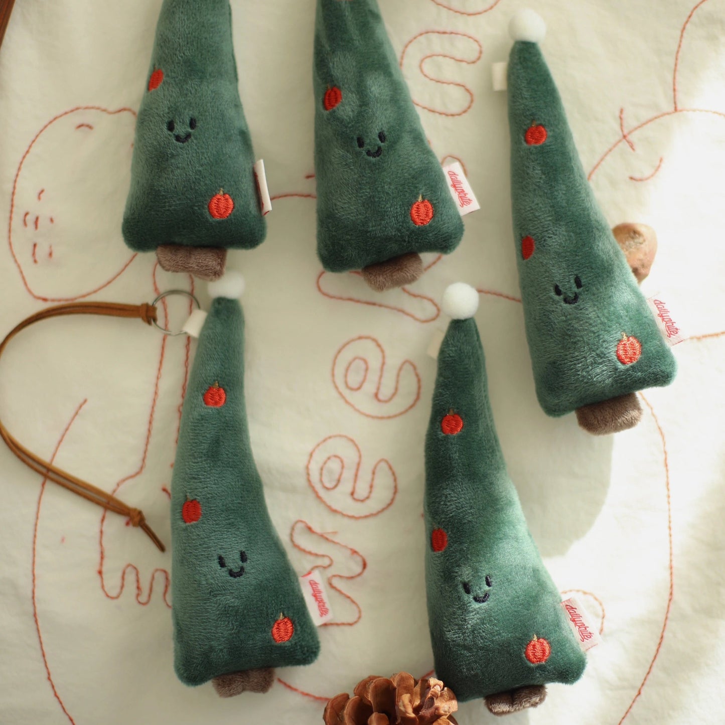 Set of green plush trees with white snowball on a textured surface with pinecones.